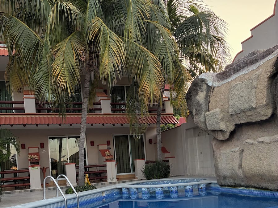 A swimming pool with a tiled edge, a palm tree, and a building with a balcony.