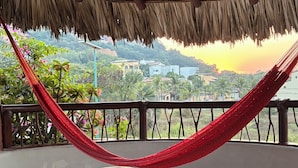 A thatched roof outdoor area with a red hammock, a table, and chairs.