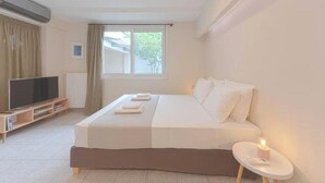Een slaapkamer met een bed, een televisie, een raam en een nachtkastje met een lamp.