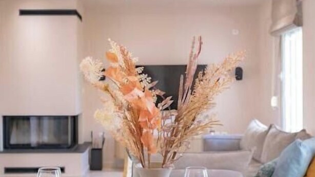 Een moderne eetruimte met een houten tafel voor vier personen, een vaas met gedroogde bloemen en een bank op de achtergrond.