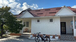 A two-story house with a tiled roof, a front porch with steps, and a bicycle parked outside.