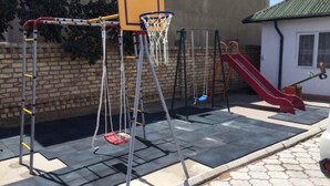 A playground with a basketball hoop, swings, and a slide.