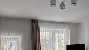 A bedroom with a bed, a TV on a stand, a window with curtains, and a view of the outside.