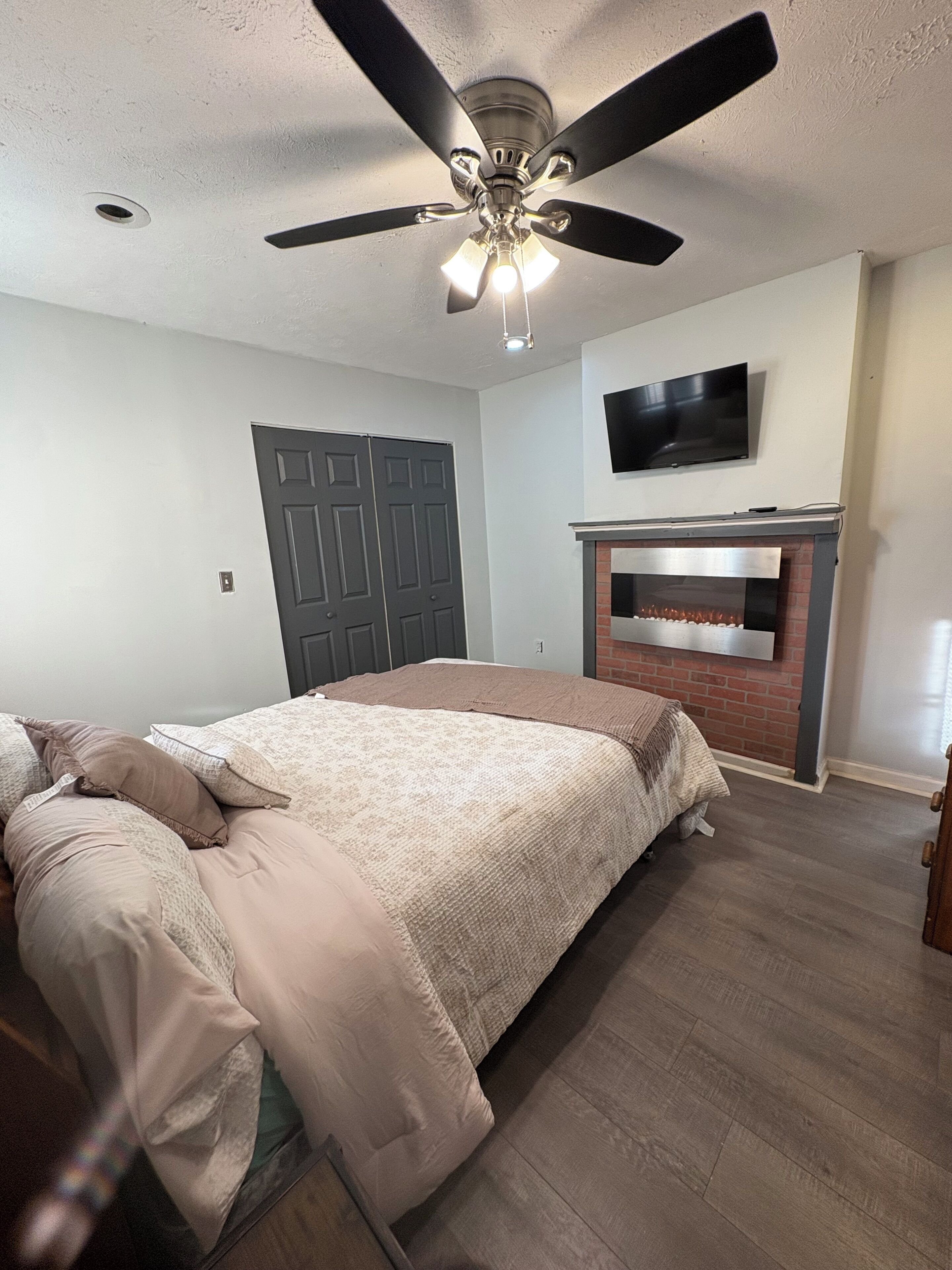 Une chambre à coucher avec un lit, un ventilateur de plafond, une cheminée et un téléviseur fixé au mur.