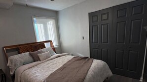 Een slaapkamer met een bed, een plafondventilator, een raam met zonwering en een deur.
