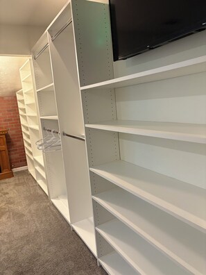 Ein Zimmer mit weißen Regaleinheiten, einem an der Wand befestigten Flachbildfernseher und einer Ziegelwand im Hintergrund.
