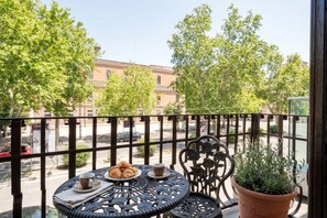 Ein Balkon mit Tisch für zwei Personen, einem Blumentopf und Blick auf die Straße und die Gebäude.