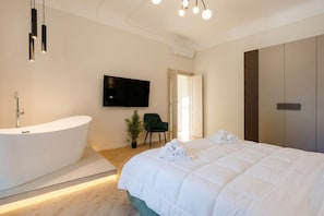 Ein modernes Schlafzimmer mit einem großen Bett, einer Badewanne, einem Flachbildfernseher und einem grünen Sessel.