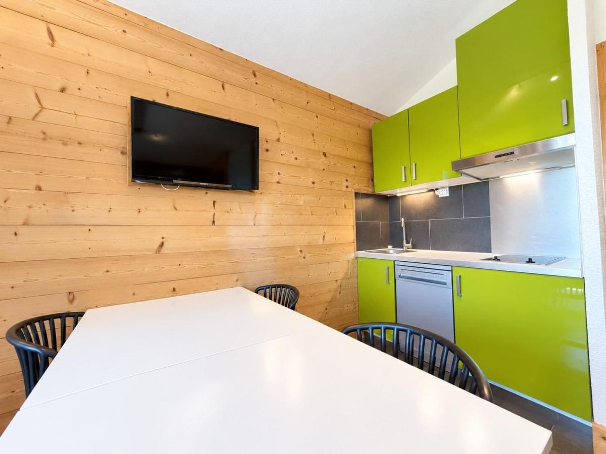 A modern kitchen with wooden walls, a flat-screen TV, and green cabinets.