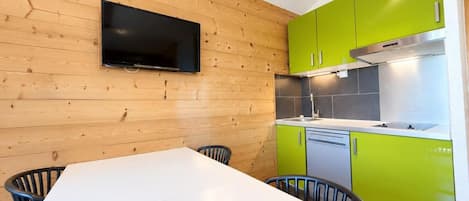 A modern kitchen with wooden walls, a flat-screen TV, and green cabinets.