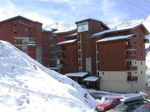 A multi-story building with wooden exterior and balconies, surrounded by snow-covered terrain. - 10m from ski slopes, 4th floor, view valley, balcony, tv, ski locker, 24m², Les Menuires (Les Menuires)