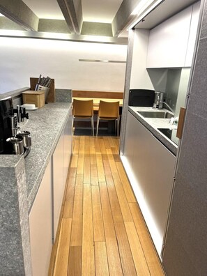 Eine schmale Küche mit Holzboden, einem Essbereich mit zwei Stühlen und einer Arbeitsplatte mit Messerblock.