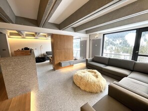 Ein modernes Wohnzimmer mit einer Eckcouch, einem flauschigen Pouf und einem eingebauten Kamin.