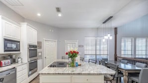 Una cocina moderna con armarios blancos, una isla central y un comedor con mesa y sillas.