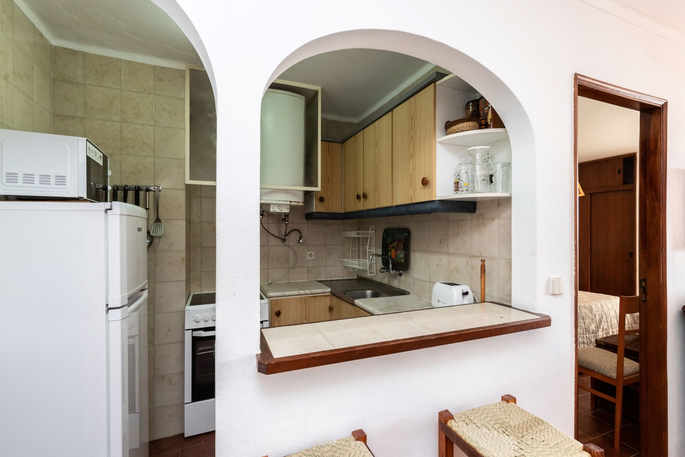 A compact kitchen with white appliances, wooden cabinets, and a built-in shelf.
