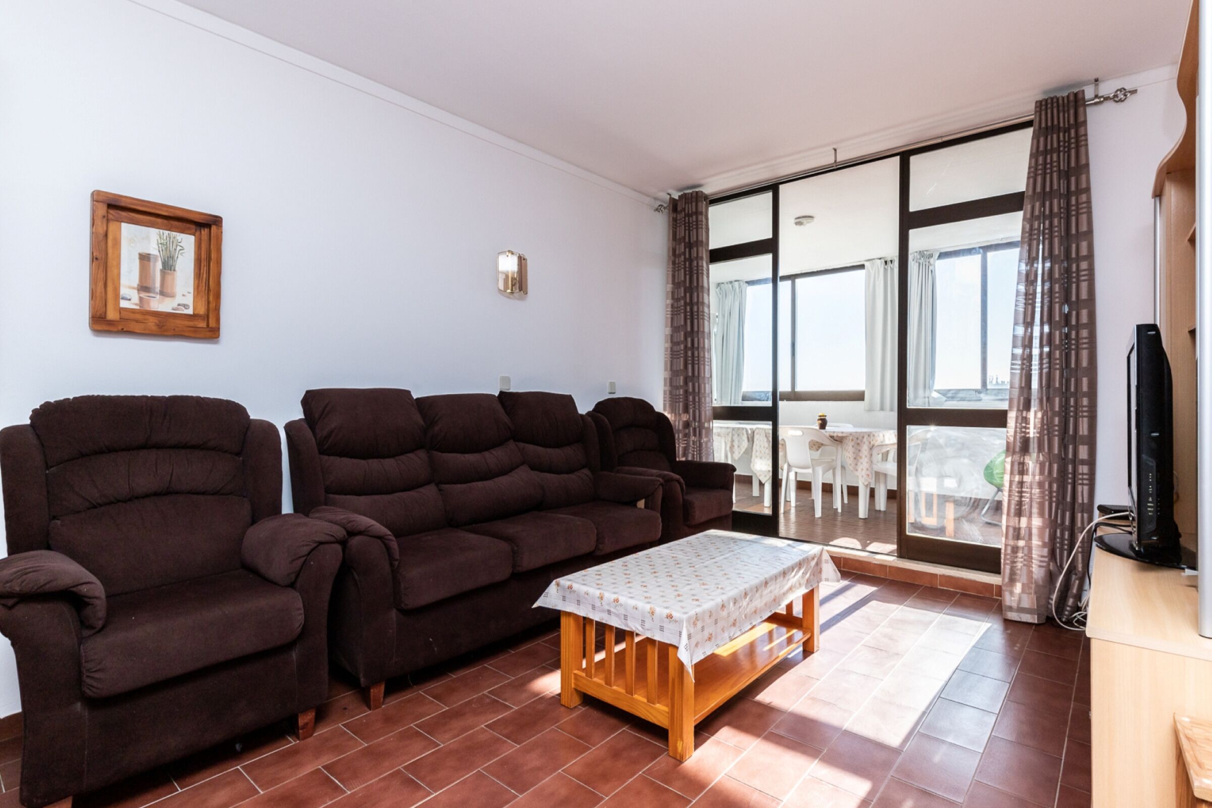 A living room with a sofa, a small table, a TV, and a sliding glass door leading to an outdoor area.