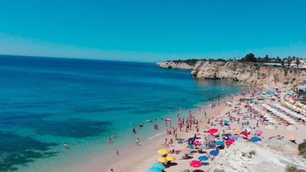 A beach with clear blue water, rocky cliffs, and umbrellas. - Sagan Brown Apartment, Armação de Pêra, Algarve (Arma ção de Pêra)