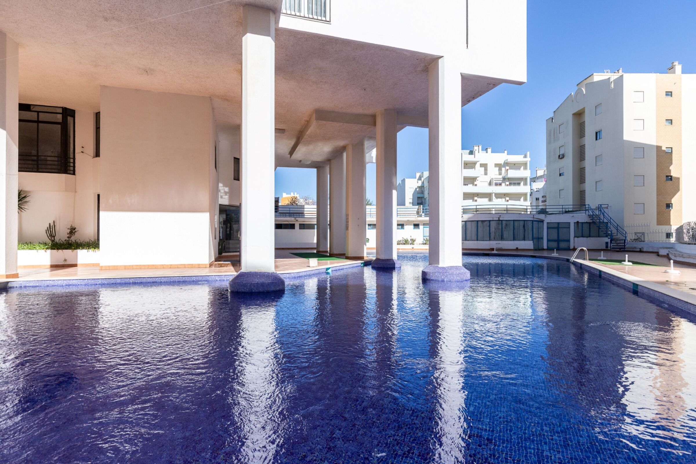 En swimmingpool med kristallklart blått vatten, omgiven av vita pelare och en modern byggnadsstruktur.