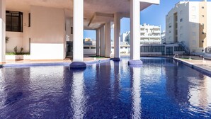 A swimming pool with clear blue water, surrounded by white pillars and a modern building structure. - Sagan Brown Apartment, Armação de Pêra, Algarve (Armação de Pêra)