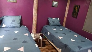 Una habitación con dos camas, una mesita pequeña y paredes moradas.