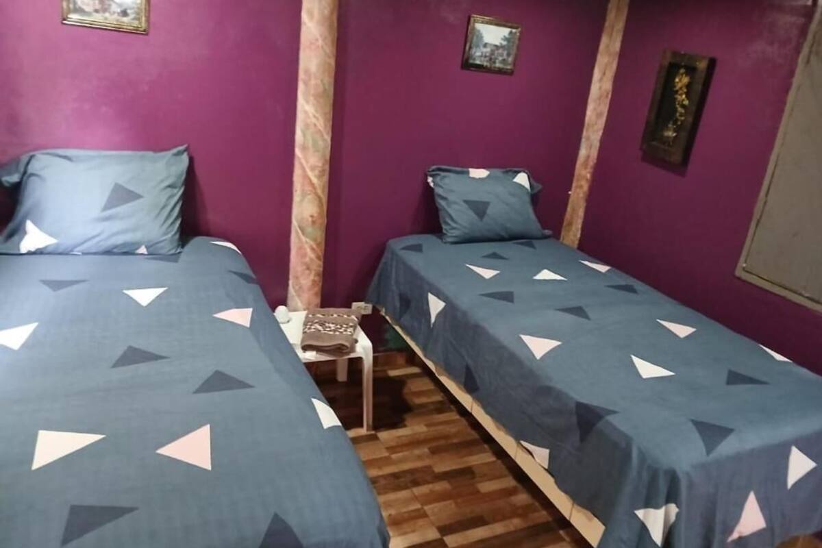 Una habitación con dos camas, una mesita pequeña y paredes moradas.