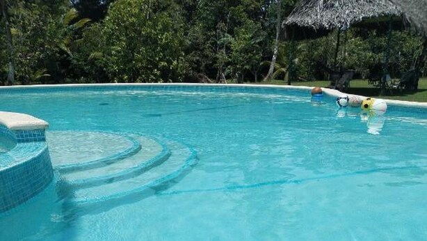 Una piscina azul clara con un parasol de paja y sillones de descanso.