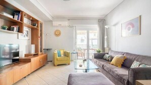 A modern living room with a sofa, a yellow armchair, a glass coffee table, and a TV on a wooden cabinet. - Casa Athenia Inn (Athina)