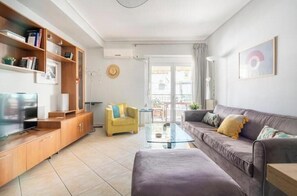 A modern living room with a sofa, a yellow armchair, a glass coffee table, and a TV on a wooden cabinet. - Casa Athenia Inn (Athina)
