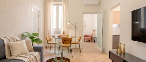 Una sala de estar moderna con un sofá, mesa de comedor, sillas, televisor y una planta.