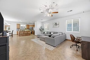 A spacious living area with a gray sectional sofa, a dining table with chairs, a kitchen in the background, and a ceiling fan. - Spacious Group Stay w/ Dual Kitchens (Bakersfield)