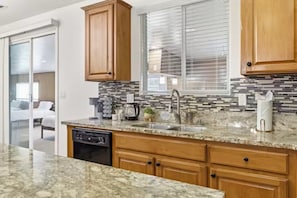 A modern kitchen with wooden cabinets, a granite countertop, and a window with blinds. - Spacious Group Stay w/ Dual Kitchens (Bakersfield)