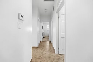 A hallway with white walls and a tiled floor, leading to a room with a window. - Spacious Group Stay w/ Dual Kitchens (Bakersfield)
