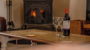 Una mesa de madera con una botella de vino y dos copas, una estufa antigua al fondo y un candelabro a la izquierda.