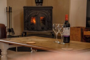 Een houten tafel met een wijnfles en twee glazen, een oude fornuis op de achtergrond, en een kandelaar aan de linkerkant.