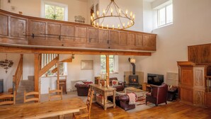 Amplia sala de estar estilo loft con una escalera de madera, chimenea, candelabro y televisión.
