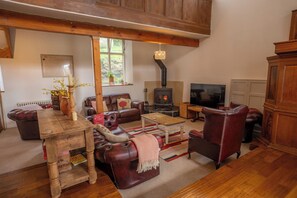 A cozy living room with a fireplace, leather sofas, a wooden coffee table, and a television. - Stunning Converted Church Near Rothbury & Cragside (Rochester)
