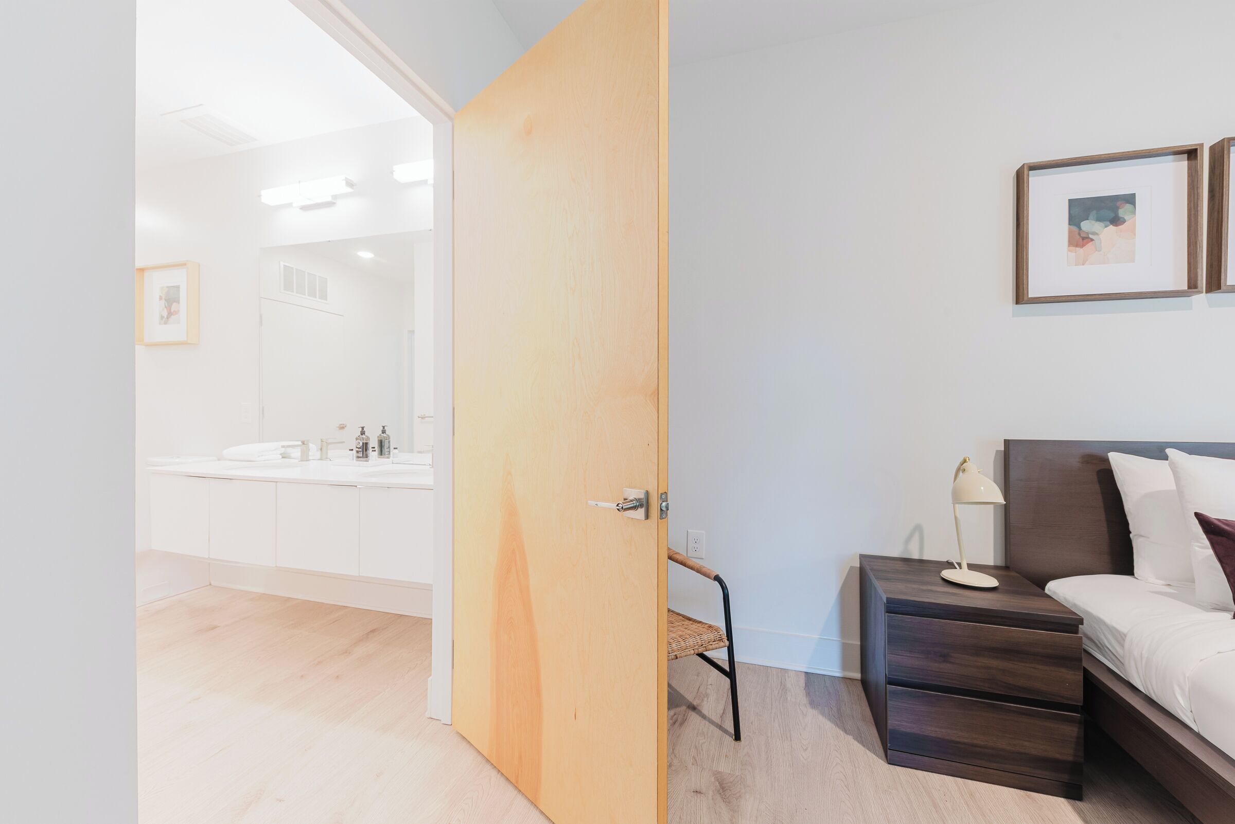 A room with a wooden door, a bed with a headboard, a bedside table, and a framed picture on the wall.