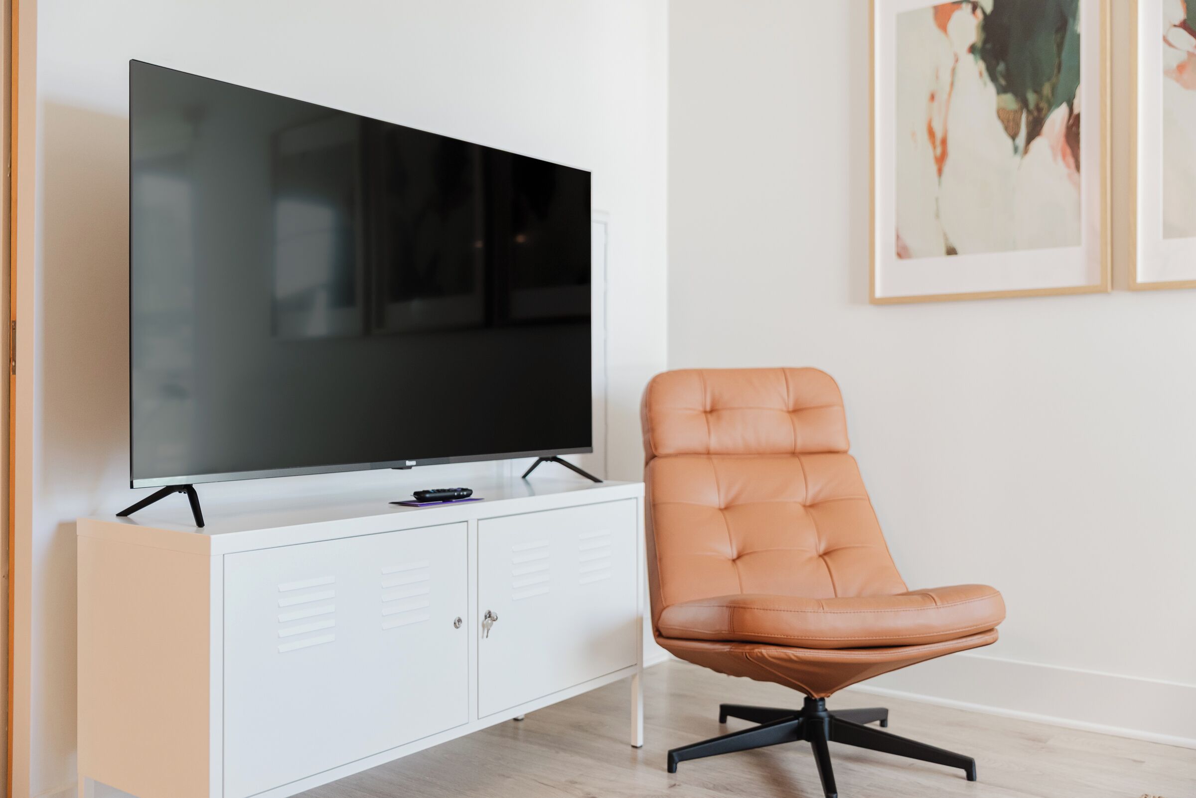 Una sala de estar moderna con un televisor de pantalla plana sobre un mueble blanco, un sillón de cuero y arte abstracto en la pared.