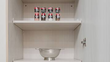 A kitchen cabinet with shelves, a colander, a glass bowl, and a frying pan.