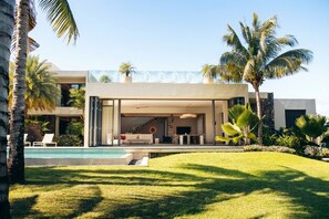 Ein modernes Haus mit Pool, Sitzgelegenheiten im Freien und Palmen.