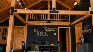 Un intérieur rustique avec des poutres apparentes, un coin repas et une enseigne indiquant « THE BURROW COFFEE BAR ».