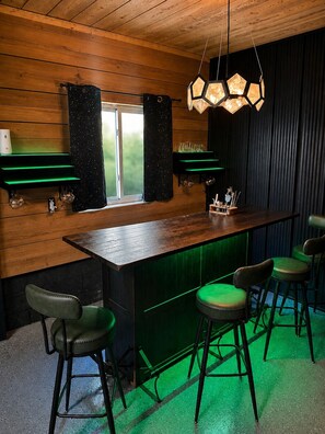 Una zona de bar con paneles de madera, una lámpara hexagonal y taburetes verdes.