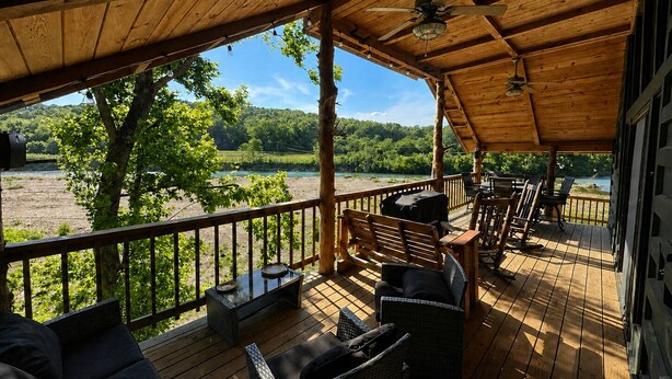 Un espace extérieur aménagé, abrité et doté de mobilier en bois, offrant une vue sur une rivière et la verdure environnante.
