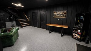 Un bar situé au sous-sol, avec une table en bois, un canapé en cuir vert, un escalier et un panneau mural.