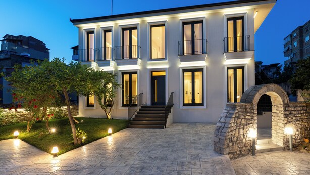 A multi-story building with a stone archway entrance, a well-lit driveway, and a small garden area.