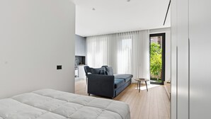 A modern hotel room with a bed, a sofa, a small table, and a view of the outdoors.