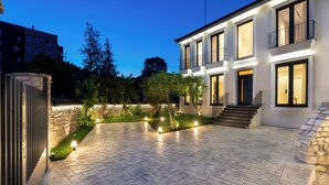 A courtyard with a stone floor, a white building with multiple windows and balconies, and a stone wall.