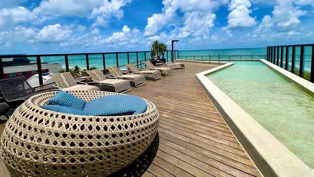 A wooden deck with lounge chairs and a pool, overlooking a clear blue sea and sky. - Restinga 11 · Beachfront apartment in Caribessa with private balcony (João Pessoa)