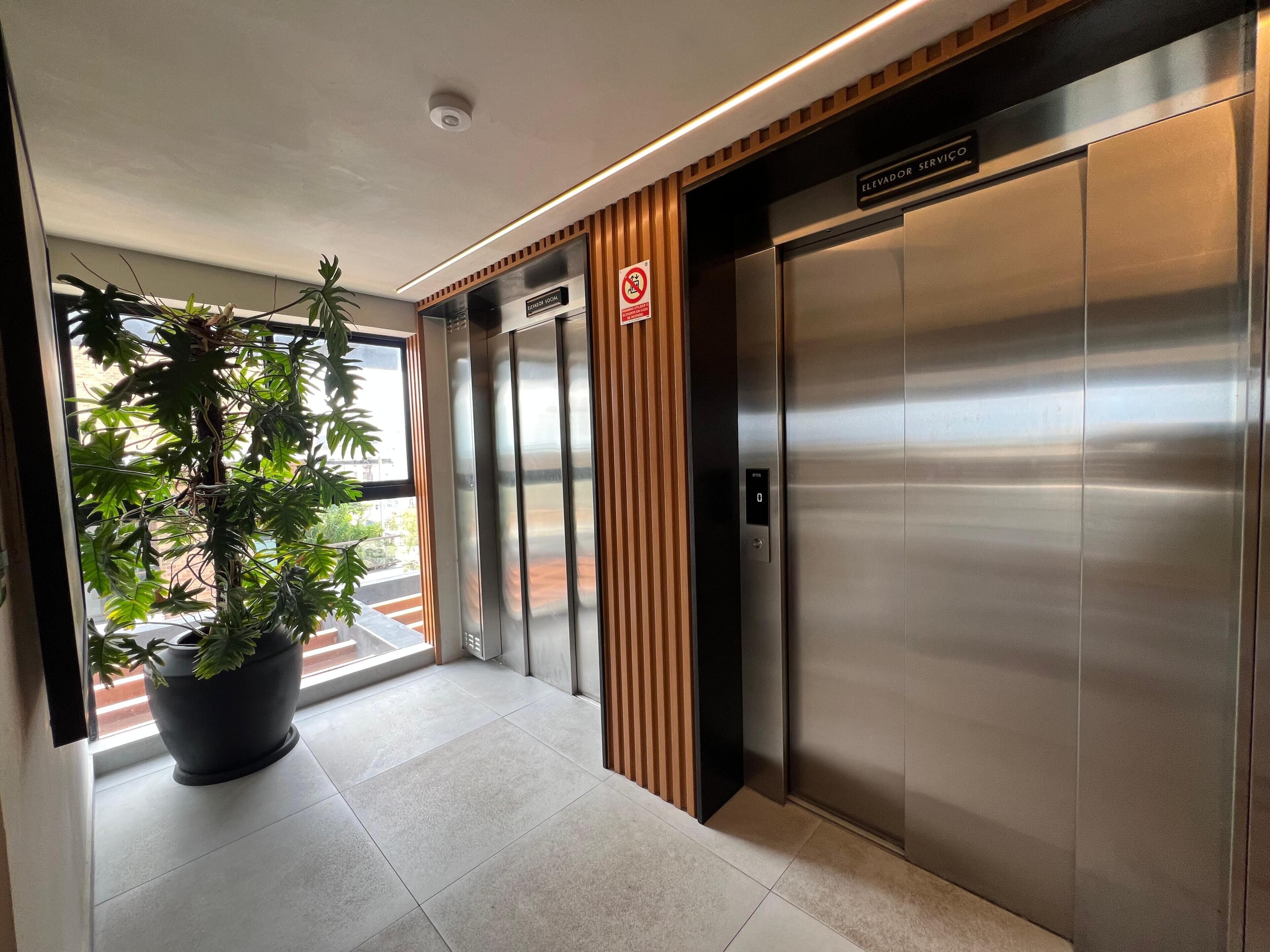 An elevator with a digital display, a sign for elevator service, and a potted plant in a modern lobby.