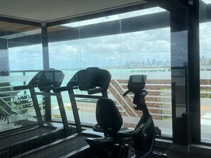 Ein Fitnessstudio mit Trainingsgeräten und Blick auf eine Skyline durch große Fenster.